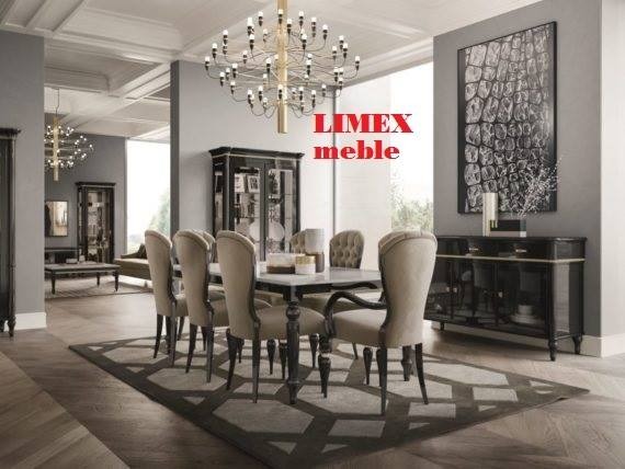 Elegancka jadalnia z owalnym stołem i krzesłami tapicerowanymi w beżowej tkaninie, oświetlona dekoracyjnym żyrandolem, z czarną komodą i abstrakcyjnym obrazem w tle.