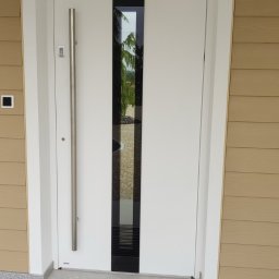 OTWARCI SPÓŁKA Z OGRANICZONĄ ODPOWIEDZIALNOŚCIĄ - Białe drzwi zewnętrzne z długim, srebrnym uchwytem i czarnym, pionowym panelem szklanym, zamontowane w domu z beżową elewacją. Wyłożone kamieniem wejście.