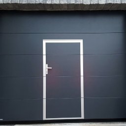 OTWARCI SPÓŁKA Z OGRANICZONĄ ODPOWIEDZIALNOŚCIĄ - Nowoczesna, antracytowa brama garażowa segmentowa z drzwiami serwisowymi i srebrnym obramowaniem, wkomponowana w kamienną elewację budynku.