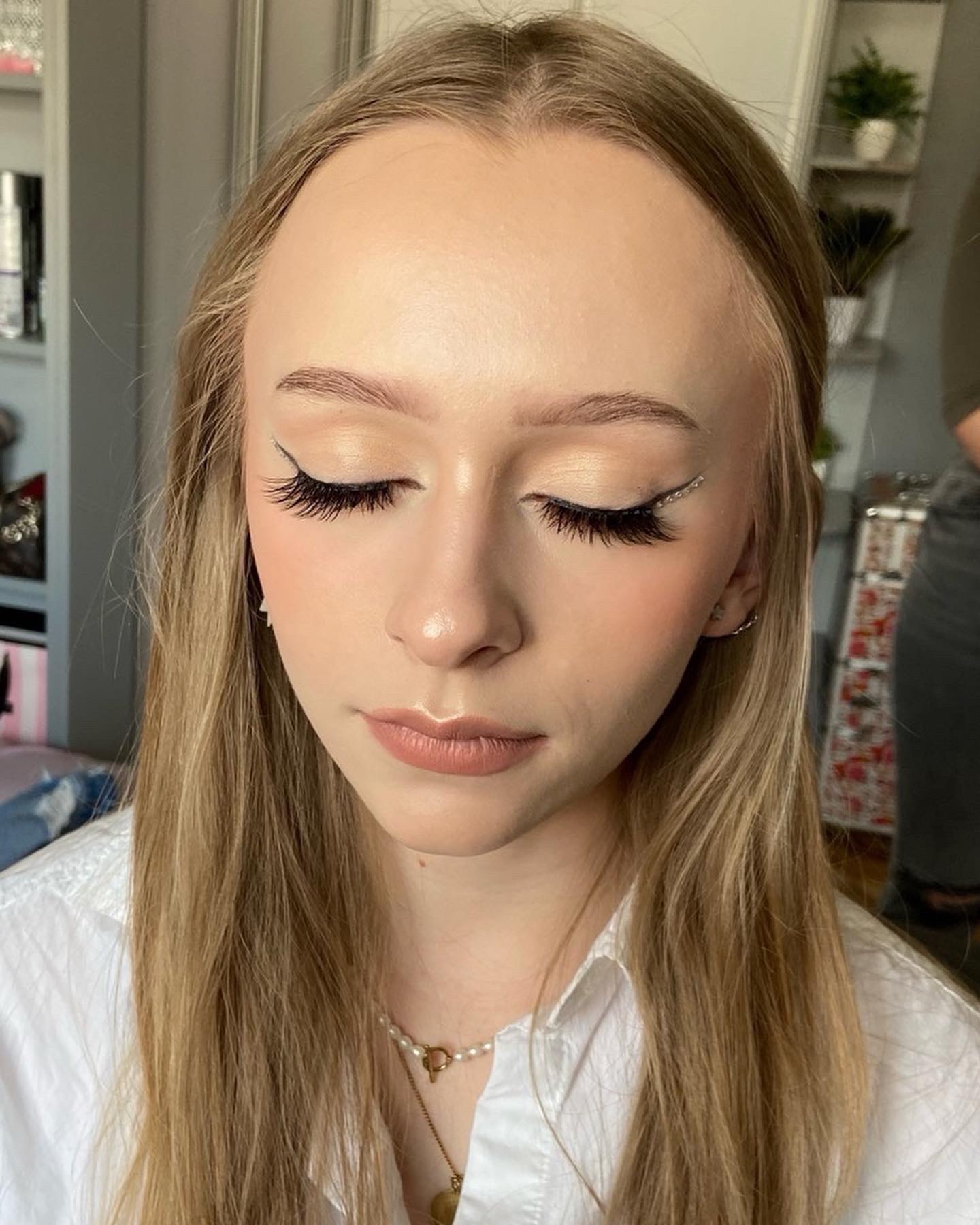 Portret kobiety z zamkniętymi oczami prezentujący delikatny, dzienny make-up z akcentem na rzęsy i subtelny eyeliner ozdobiony błyszczącymi kamyczkami.