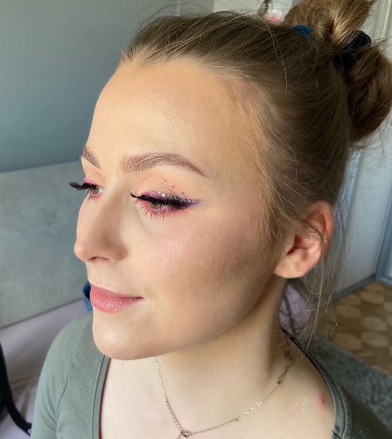 Profil kobiety z delikatnym makijażem w odcieniach różu i fioletu, brokatowy eyeliner z drobnymi kamyczkami, wykonany w Warszawie.