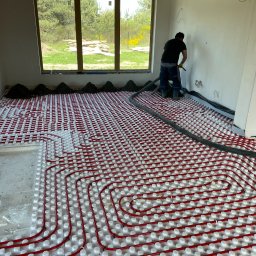 Milke Wykończenia - Pracownik w trakcie wylewki posadzki na ogrzewanie podłogowe w nowym domu z dużymi oknami.