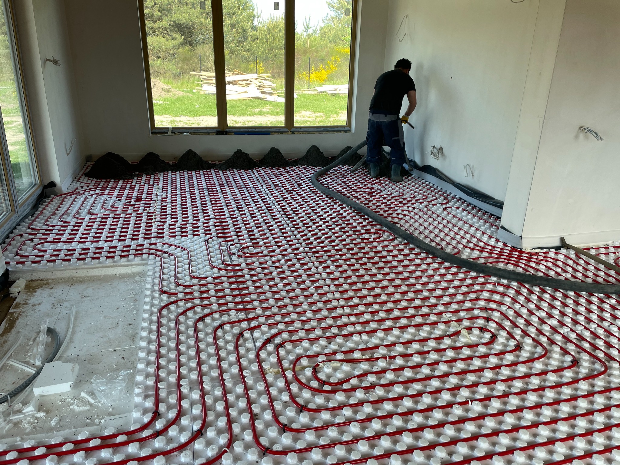 Pracownik w trakcie wylewki posadzki na ogrzewanie podłogowe w nowym domu z dużymi oknami.
