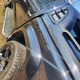 Błyszczący, ciemny samochód terenowy z chromowanymi progami, sfotografowany pod kątem, ukazujący odbicie drzew w karoserii.