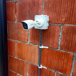 Kamera monitoringu Hikvision zamontowana na czerwonej ścianie z cegły, przewody zabezpieczone opaskami zaciskowymi.