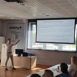 Prelegent w jasnej koszuli i spodniach gestykuluje podczas prezentacji na temat obniżki podatku z 17% na 12%, wyświetlanej na ekranie projektora w sali konferencyjnej Poznańskiego Parku...