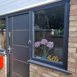 Homeefe Ltd - Ciemnoszare drzwi wejściowe z przeszkleniem bocznym i oknem, skrzynka pocztowa w kolorze czerwonym, widok z zewnątrz.