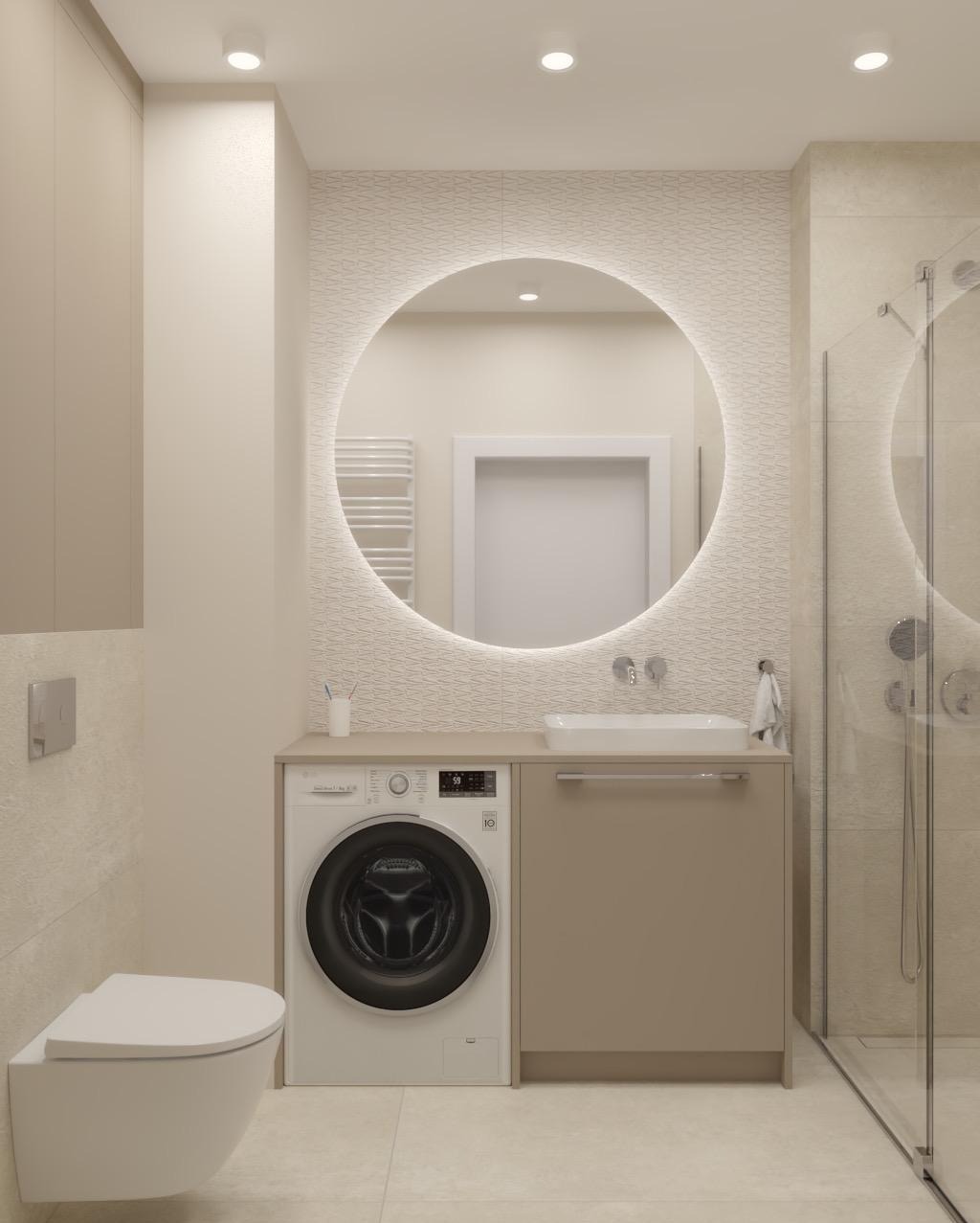 Jasna łazienka z okrągłym lustrem z podświetleniem LED, toaletą podwieszaną i pralką w zabudowie. Minimalistyczny design, beżowa kolorystyka, kabina prysznicowa.
