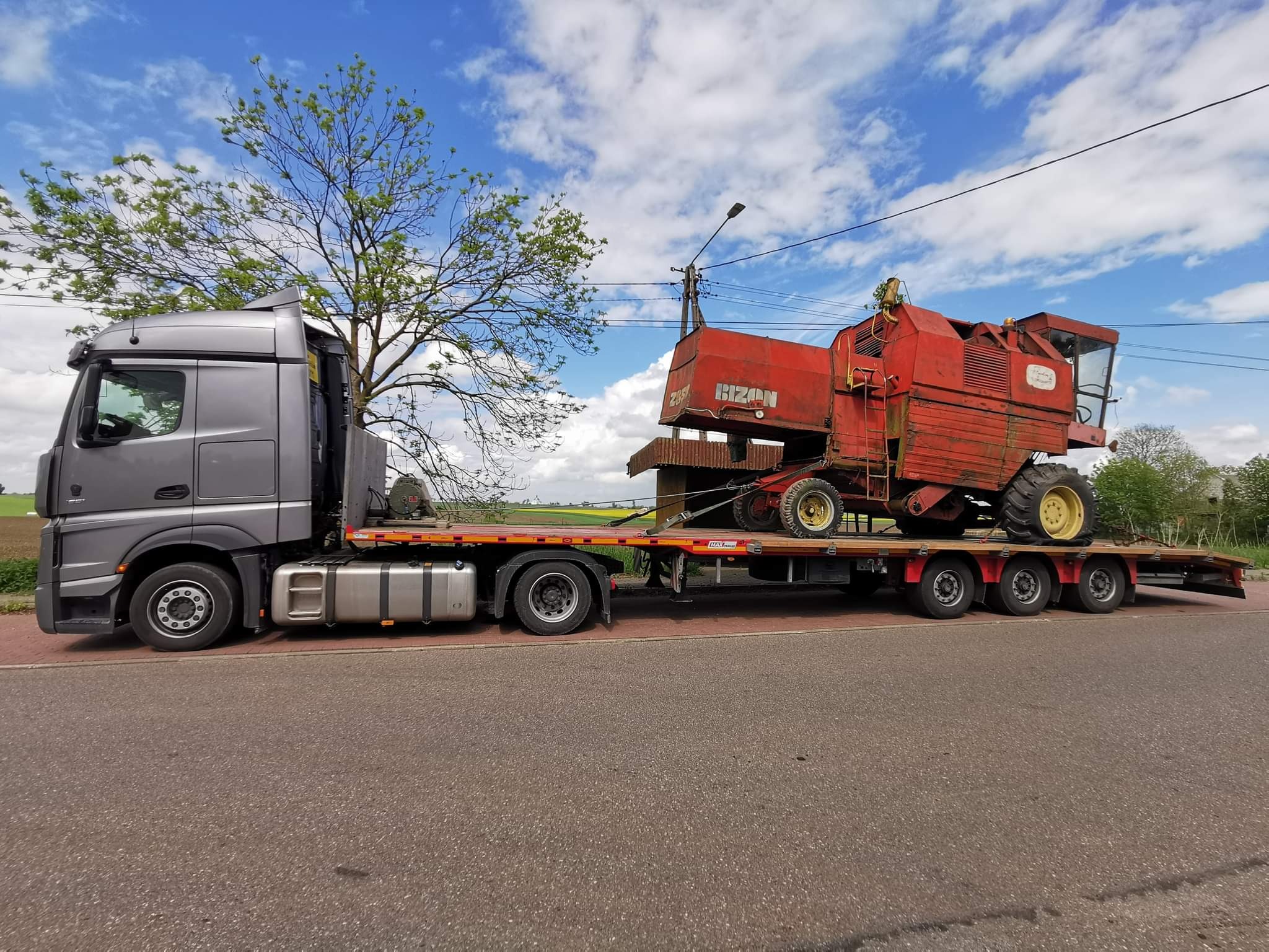 Ciężarówka transportuje kombajn zbożowy Bizon na niskopodwoziowej platformie w słoneczny dzień.