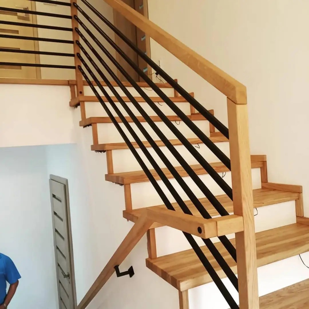 Drewniane schody z czarnymi metalowymi balustradami, widok z dołu, jasne drewno stopni i poręczy, minimalistyczny design.
