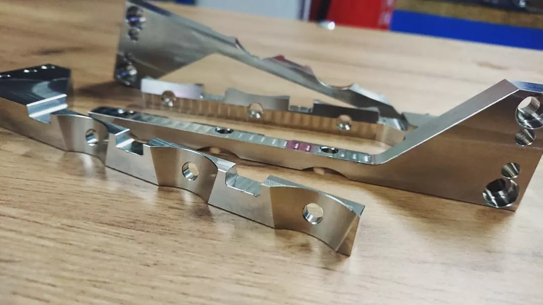 Precyzyjnie obrobione, metalowe elementy z otworami, leżące na drewnianym stole, widoczne ślady obróbki skrawaniem.