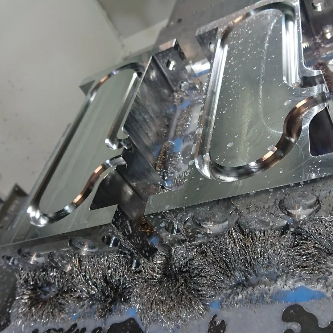 Precyzyjnie obrobiony metalowy element z widocznymi śladami frezowania i chłodziwa, leżący na stole maszyny wśród wiórów.