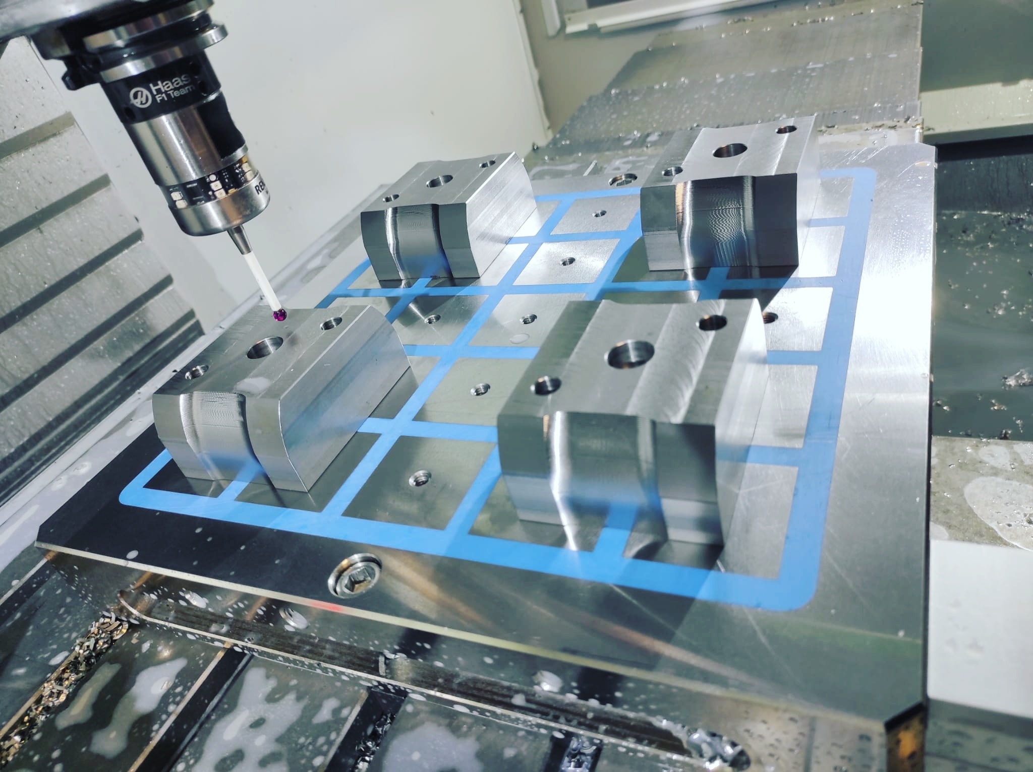 Precyzyjny pomiar metalowych bloków z otworem za pomocą sondy pomiarowej w maszynie CNC, widoczne wióry i chłodziwo.