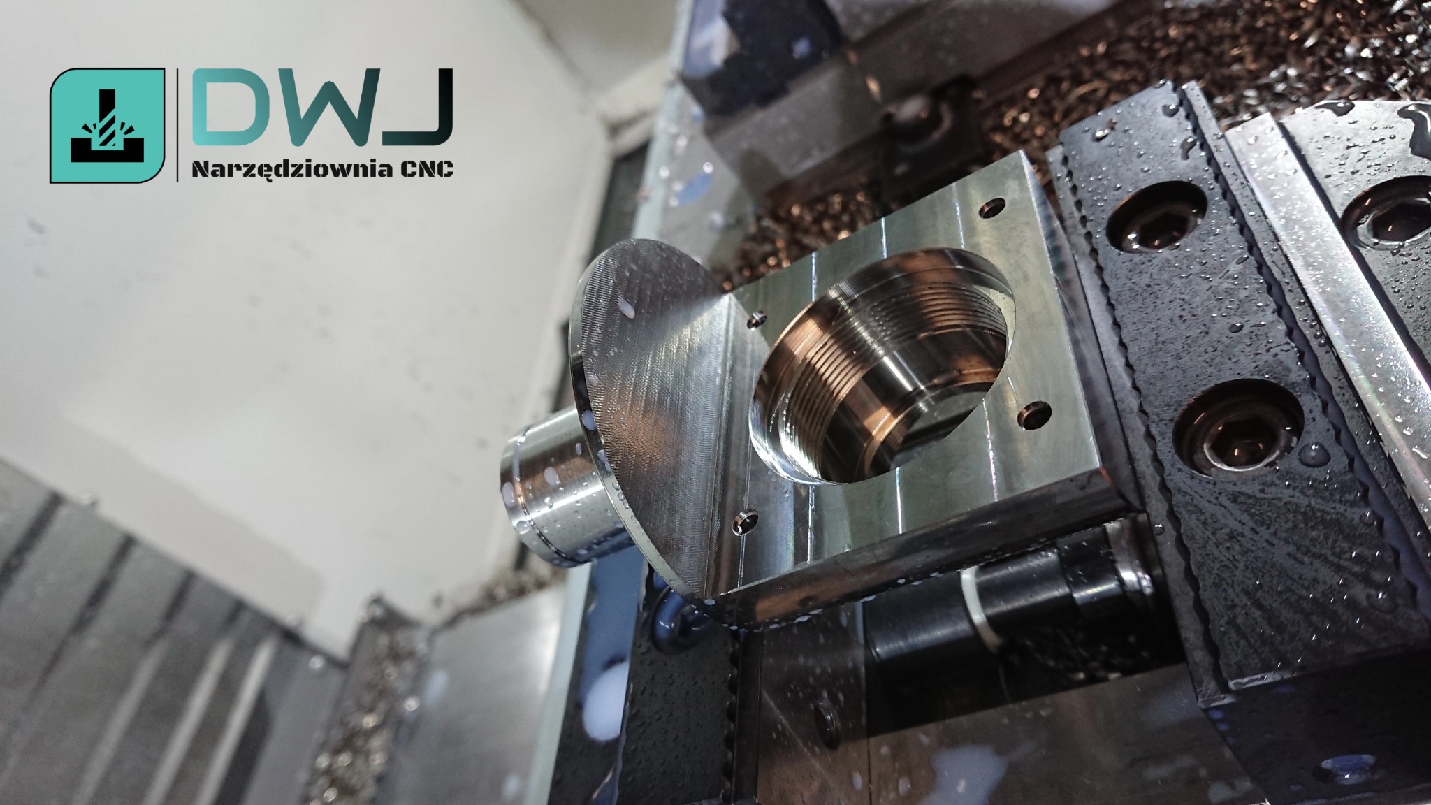 Obrabiany element z gwintem wewnętrznym zamocowany w uchwycie tokarki CNC, widoczne wióry i płyn chłodzący.