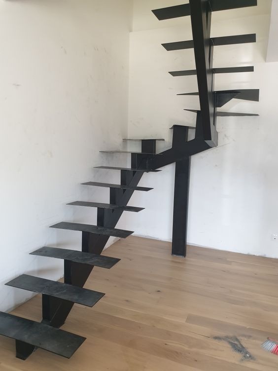 Nowoczesne, metalowe schody o minimalistycznym designie, z czarnymi stopniami i centralną podporą, zamontowane w jasnym wnętrzu z drewnianą podłogą.