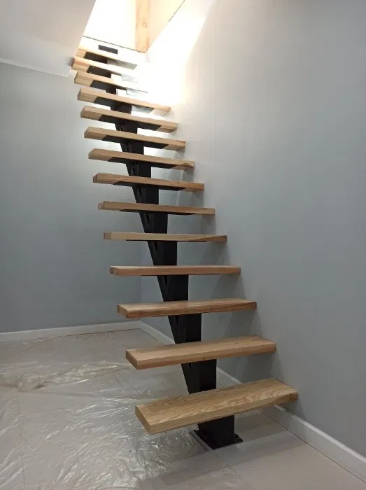 Nowoczesne schody z drewnianymi stopniami i metalową konstrukcją nośną, widok z dołu, podłoga zabezpieczona folią malarską.