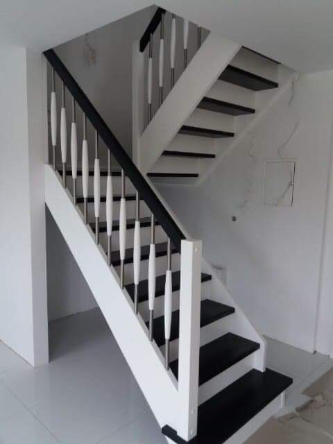 Schody drewniane dwubiegowe z czarnymi stopniami i białymi barierkami z ozdobnymi, toczonymi elementami, widok z dołu na wprost.