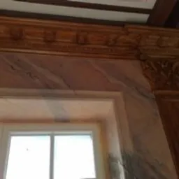 Ściana z efektem marmoryzacji, widoczna kolumna dekoracyjna i sztukateria pod sufitem, okno w dolnej części kadru, imitacja marmuru w odcieniach różu i szarości.