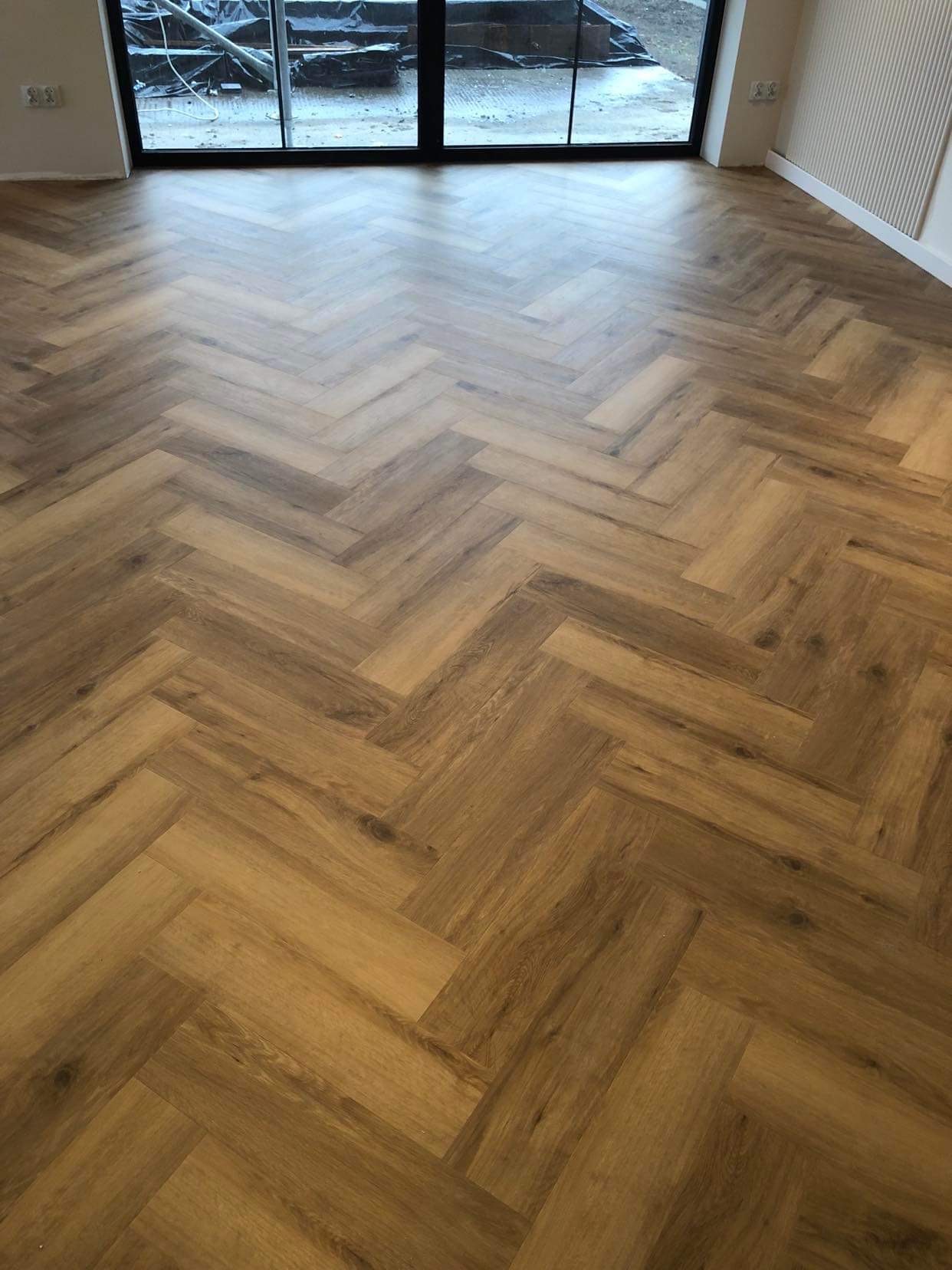 Ułożona w jodełkę podłoga z paneli imitujących drewno, widok z góry w jasnym pomieszczeniu z dużym oknem.