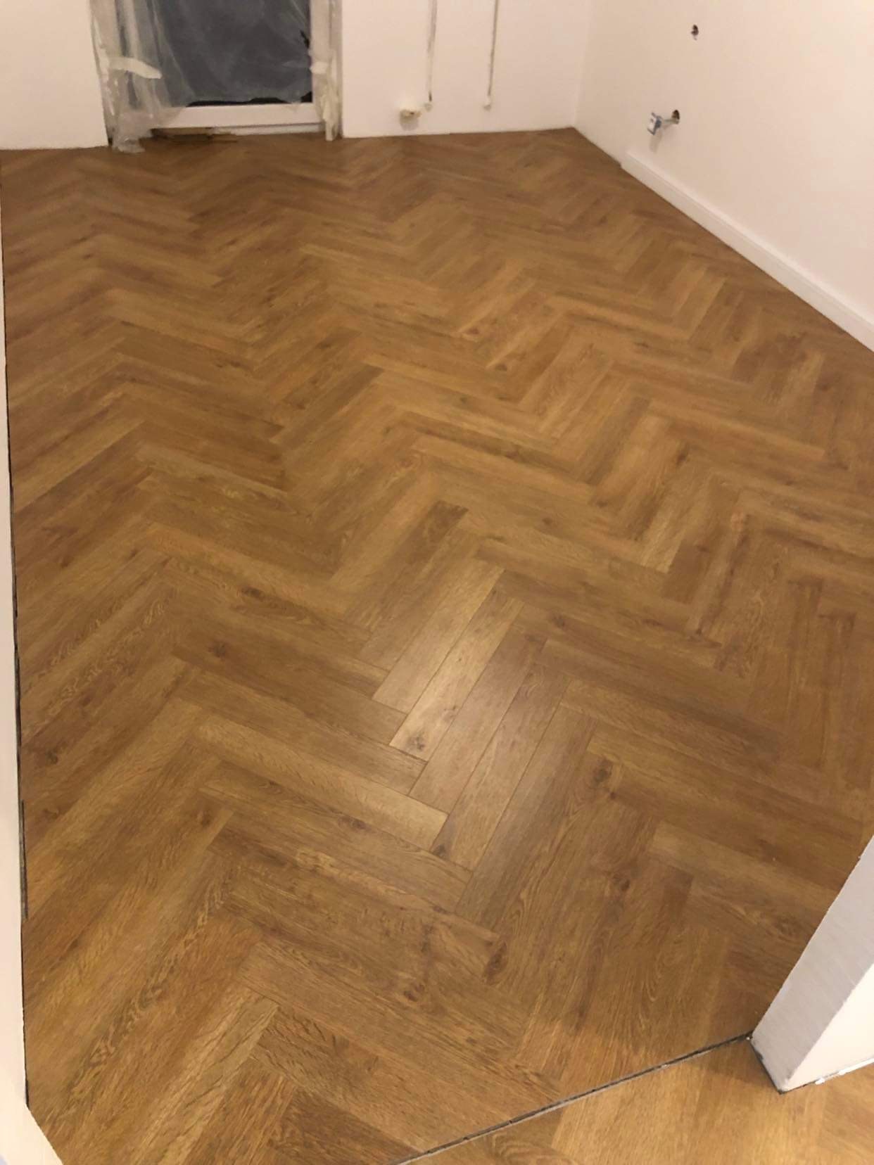 Ukończona podłoga z paneli ułożonych w jodełkę w nowym pomieszczeniu, widoczne niedoskonałości wykończenia przy ścianach.