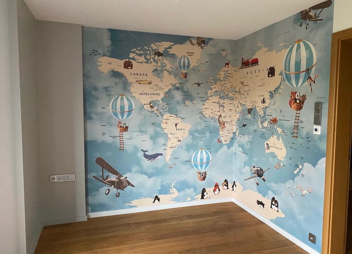 Pokój dziecięcy z fototapetą przedstawiającą mapę świata z motywami zwierząt, samolotów i balonów, drewniana podłoga.