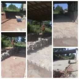 Układanie kostki brukowej w zadaszonej przestrzeni: widok na częściowo ułożoną nawierzchnię z szarej kostki, stosy kostki przygotowanej do ułożenia oraz taczkę w tle.