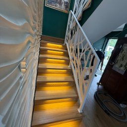 Usługi Stolarskie Lofthomeland Jakub Korzeniowski - Nowoczesne schody drewniane z podświetleniem LED i białą, ażurową balustradą w Trzeszczynie. Dekoracyjna ściana z efektem 3D. Unikalny design i precyzyjne wykonanie.