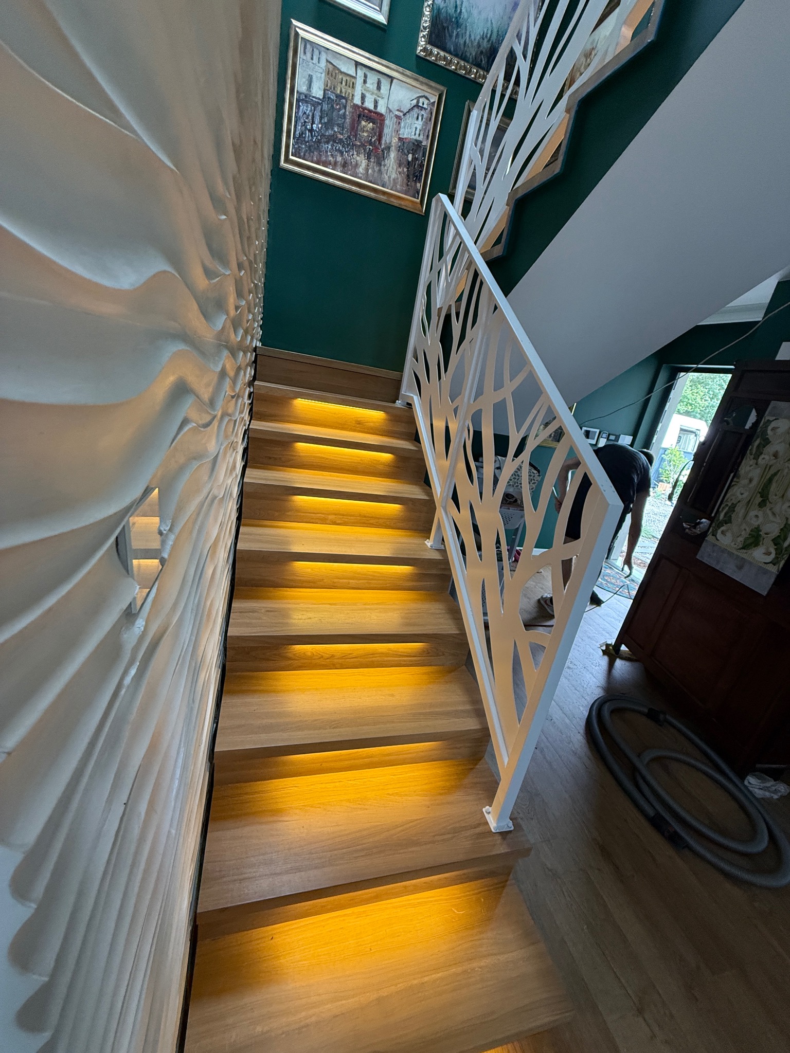 Nowoczesne schody drewniane z podświetleniem LED i białą, ażurową balustradą w Trzeszczynie. Dekoracyjna ściana z efektem 3D. Unikalny design i precyzyjne wykonanie.