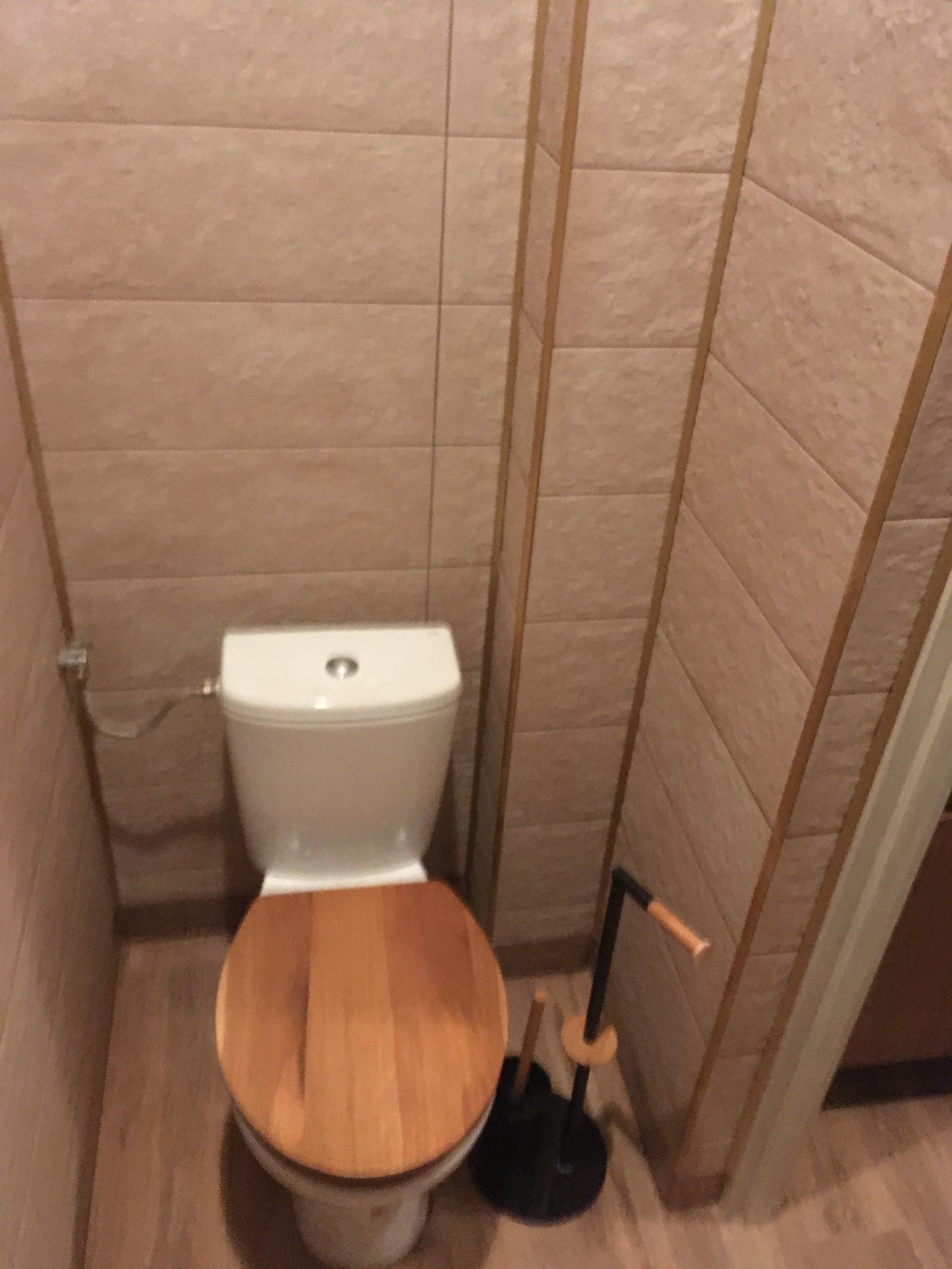 Toaleta z drewnianą deską w łazience wykończonej beżowymi płytkami, widoczna w Szczecinie, z akcesoriami łazienkowymi.