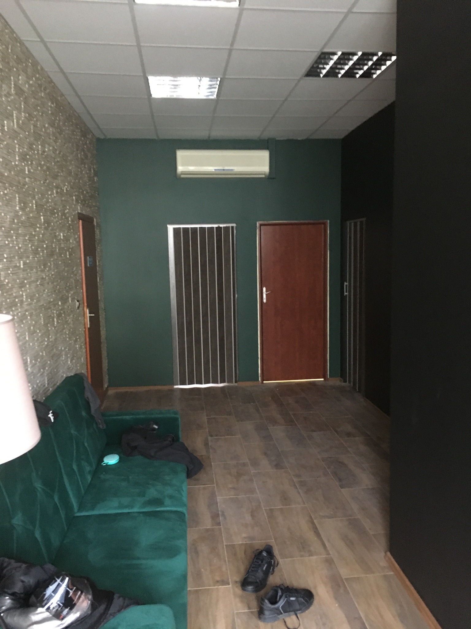 Wnętrze po remoncie: zielona ściana, brązowe drzwi, sufit kasetonowy, podłoga z płytek imitujących drewno, zielona sofa z rzeczami na niej.