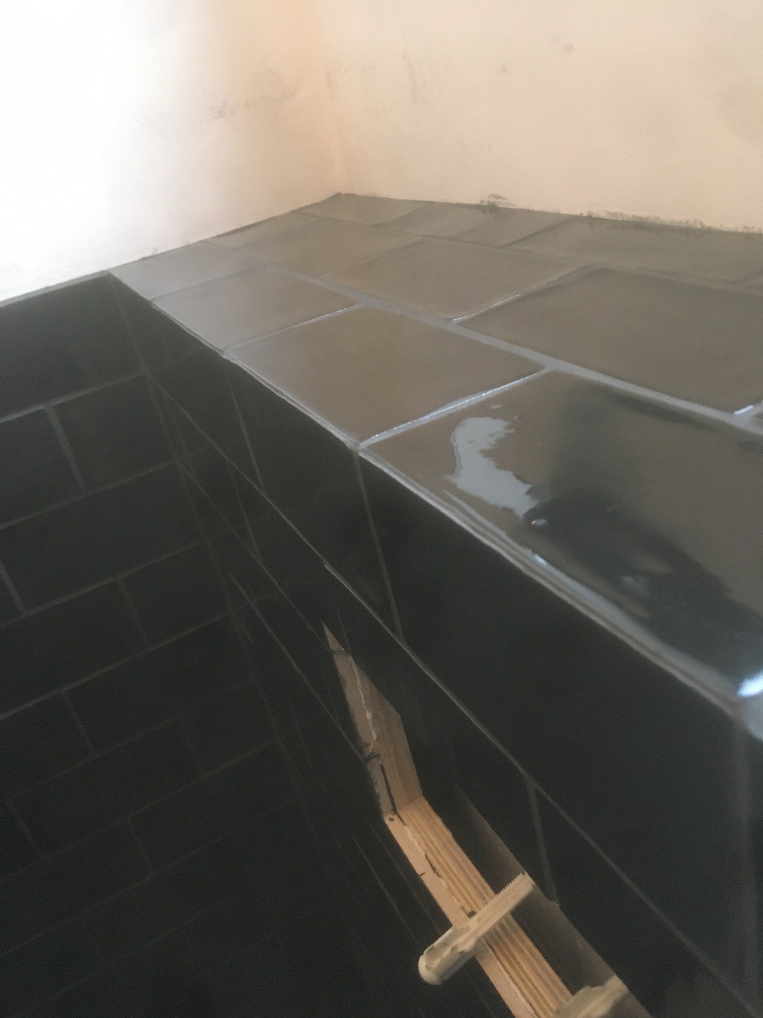 Świeżo położone, błyszczące, czarne płytki na ścianie i półce, widoczne drewniane elementy konstrukcyjne pod spodem, fuga jeszcze mokra.