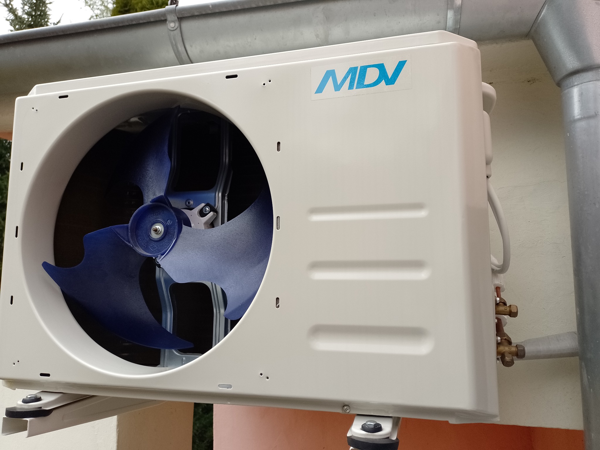 Zewnętrzna jednostka klimatyzacji MDV zamontowana na ścianie budynku w Suchej, widoczne rury i niebieskie łopatki wentylatora.