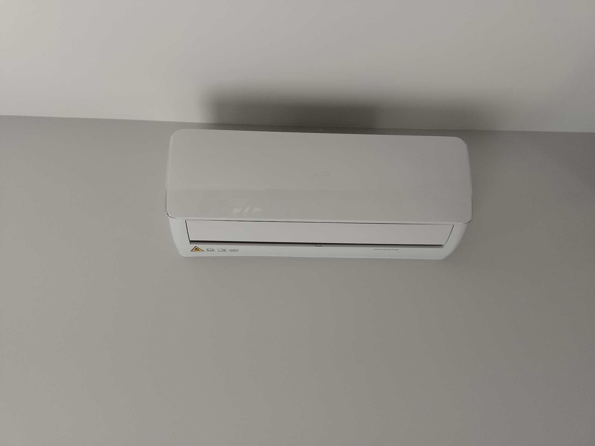 Biała klimatyzacja marki AUX zamontowana na szarej ścianie w pomieszczeniu.