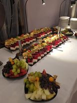 Stół z owocowymi przekąskami w Konstantynowie Łódzkim: kompozycje owocowe ułożone w geometryczne wzory na ciemnych tacach, uzupełnione miseczkami z winogronami i innymi owocami. Oświetlenie...