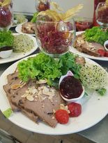 Elegancko podany talerz z pieczenią wołową posypaną płatkami migdałów, sałatą, sosem żurawinowym i dwoma truskawkami, obok zielona sałatka i kompozycja w szklanym naczyniu z buraków i dekoracji.