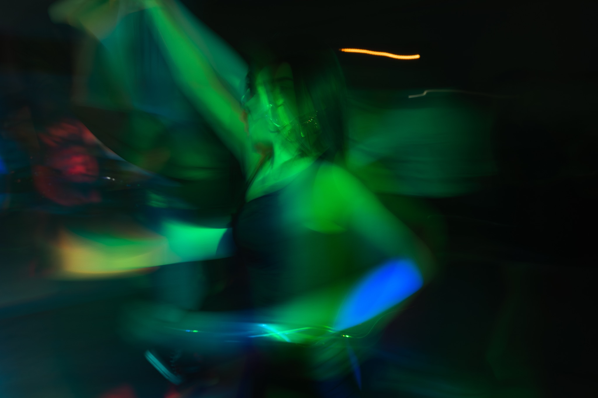 Rozmazane zdjęcie kobiety w ruchu, oświetlonej zielonym i niebieskim światłem, wykonane prawdopodobnie podczas imprezy w Radomiu.
