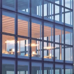 Elewacja biurowca z widocznymi biurami wewnątrz, oświetlonymi podłużnymi lampami, z perspektywą lekko od dołu.