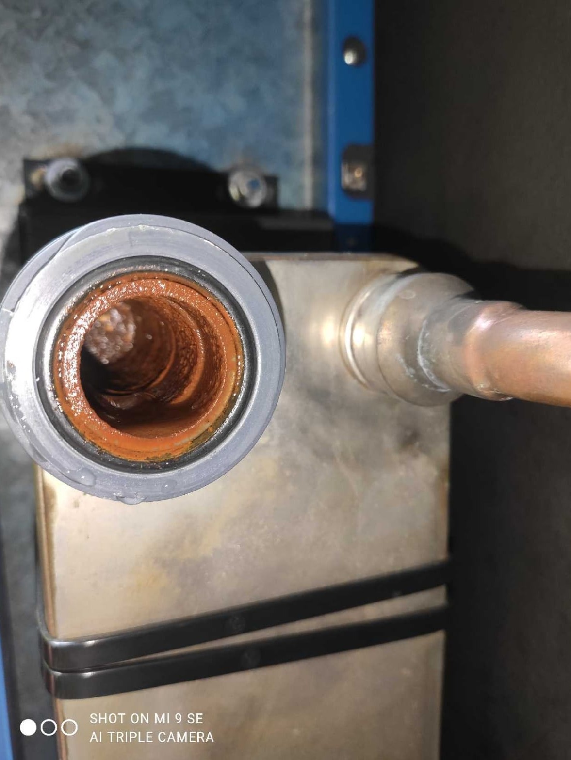 Zardzewiałe wnętrze rury odpływowej z osadem i kroplami wody, widoczne przyłącze do wymiennika ciepła