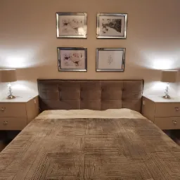 Nowoczesna sypialnia z szarym łóżkiem, tapicerowanym zagłówkiem i wiszącymi szafkami nocnymi z kryształowymi gałkami, oświetlona lampkami nocnymi i udekorowana czterema obrazami w srebrnych ramkach.