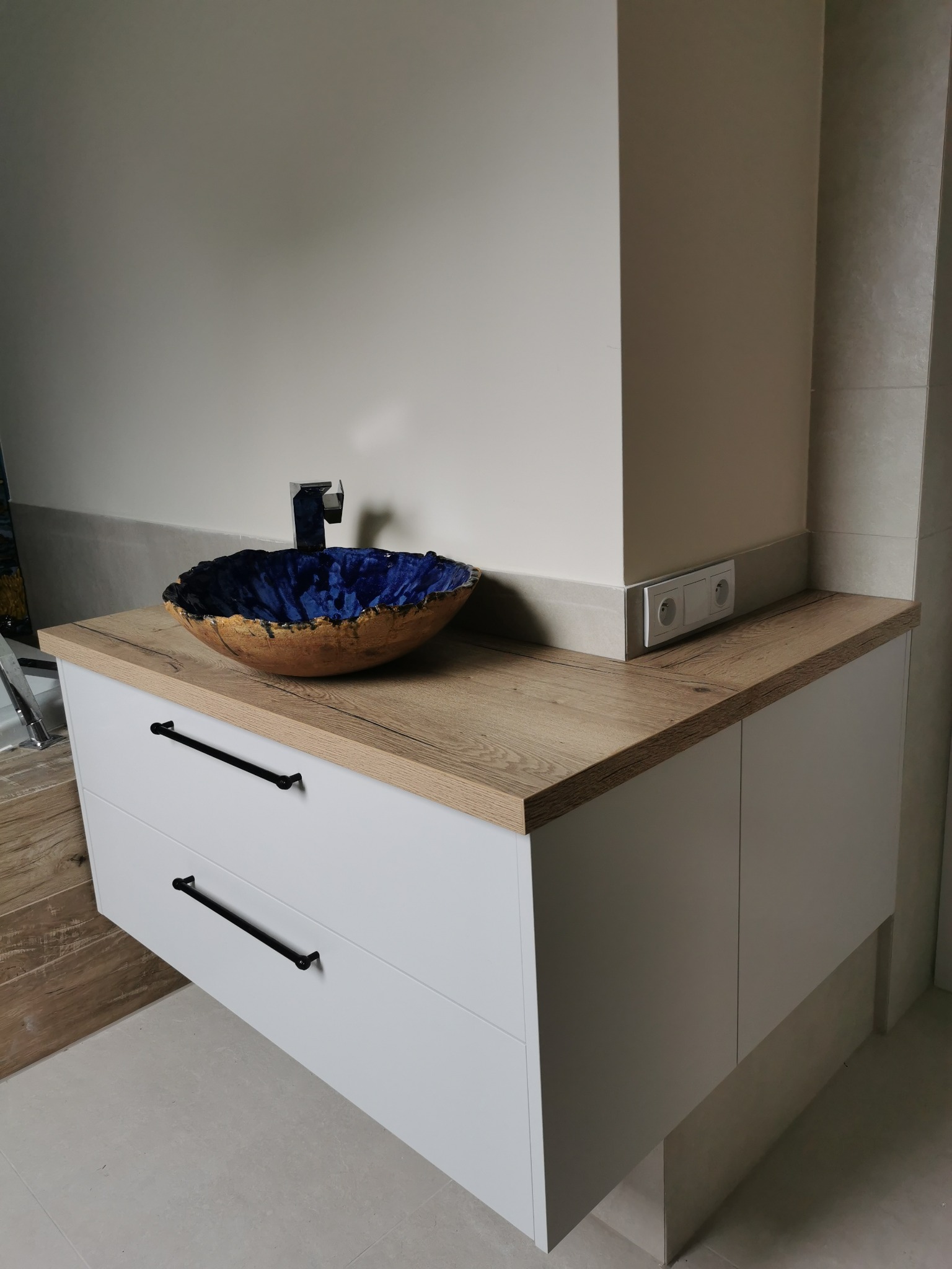 Narożna szafka łazienkowa, z dwoma szufladami i ukrytą szafeczką po prawej stronie. Wykonana z MDF lakierowanego.