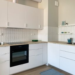 Hello Home Maja Maik - Jasna kuchnia w stylu skandynawskim: białe szafki z drewnianym blatem, pionowe płytki na ścianie, minimalistyczny wystrój i subtelny dywanik.