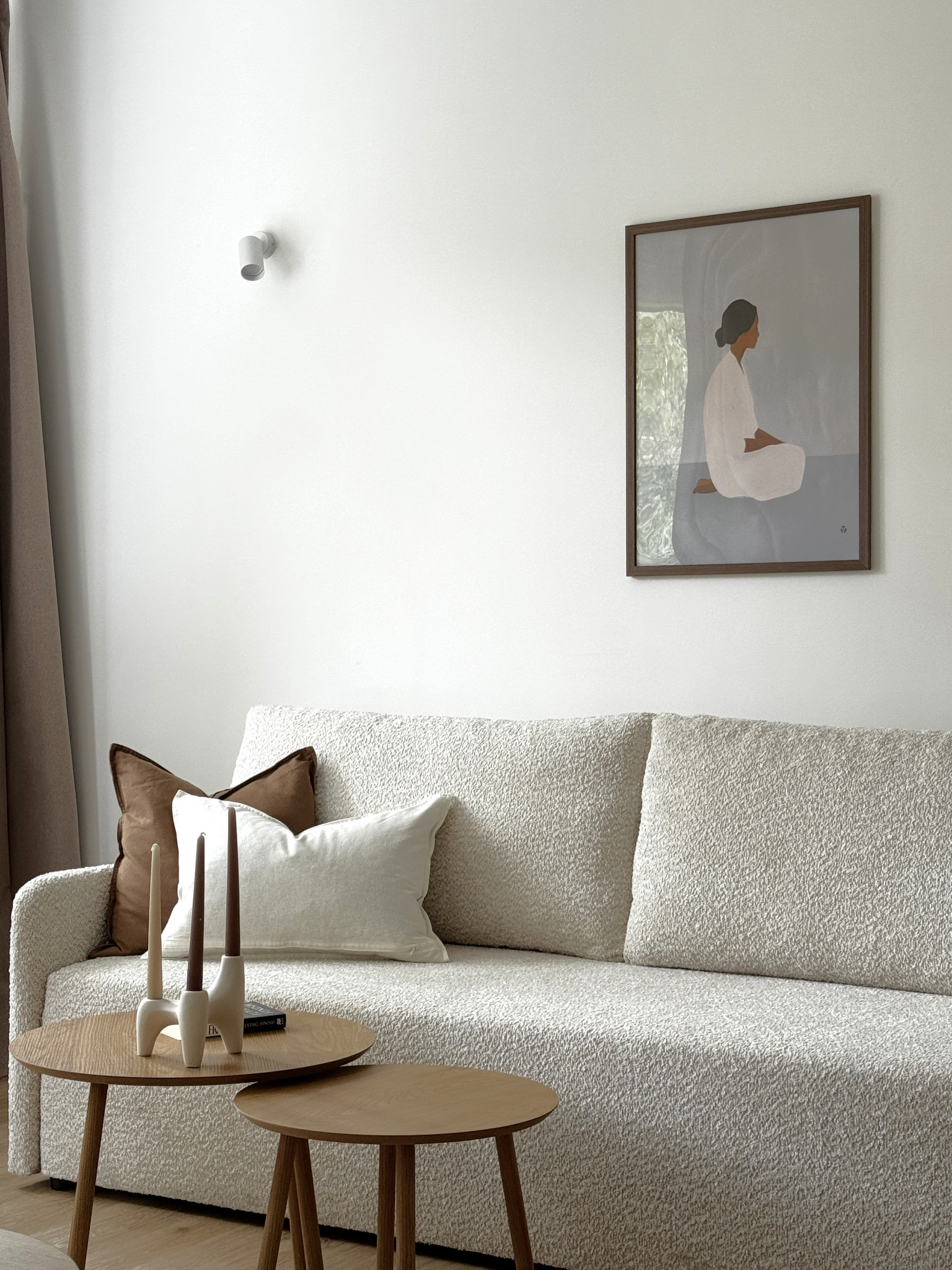 Jasny salon z teksturowaną sofą, drewnianymi stolikami kawowymi i minimalistycznym obrazem kobiety w bieli. Stonowana kolorystyka, nowoczesny design, subtelne oświetlenie.
