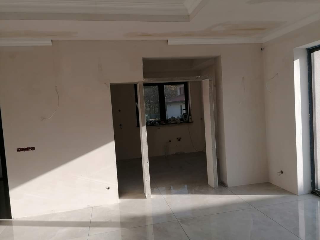 Wnętrze w trakcie remontu: ściany przygotowane do malowania, widoczne ślady po szpachlowaniu i gładzi, sufit z dekoracyjną listwą, błyszcząca podłoga z płytek, ościeżnice drzwiowe bez drzwi.