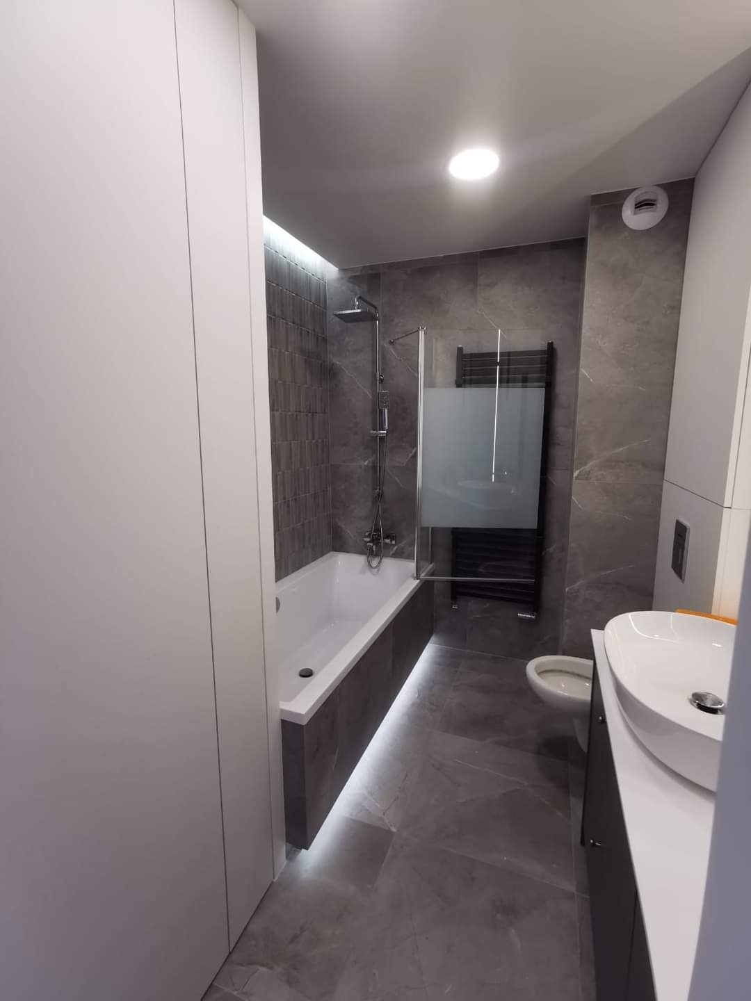 Nowoczesna łazienka w odcieniach szarości z podświetlaną wanną, kabiną prysznicową typu walk-in i umywalką nablatową na szafce.