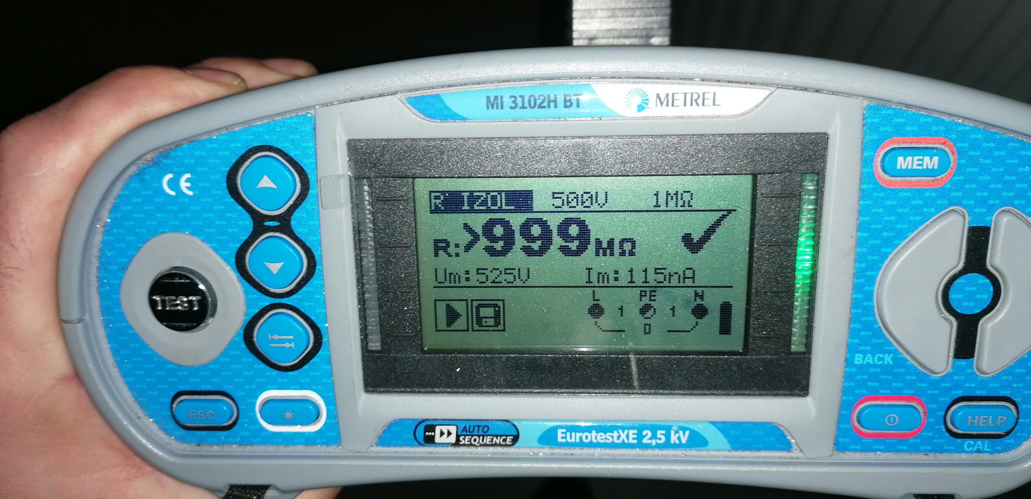 Miernik izolacji Metrel MI 3102H BT w trakcie pomiaru, wyświetlający wynik powyżej 999 megaomów z napięciem 525V, widoczny fragment dłoni operatora.