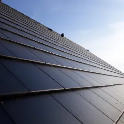 Nowoczesny dach z czarnej dachówki ceramicznej, widok pod kątem, błękitne niebo w tle.