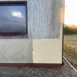 FHU Błażej Trznadel - Fragment elewacji budynku z widocznym oknem i próbką nowej farby, na tle zachodzącego słońca i zieleni.