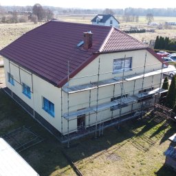 FHU Błażej Trznadel - Dom jednorodzinny w trakcie malowania elewacji, okna zabezpieczone folią, rusztowanie przy ścianie, widok z góry.