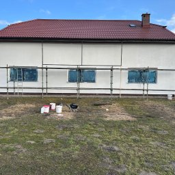 FHU Błażej Trznadel - Przygotowania do prac elewacyjnych w Sianowie: dom z zabezpieczonymi oknami, rusztowanie, wiaderka z farbą i agregat malarski na trawniku.