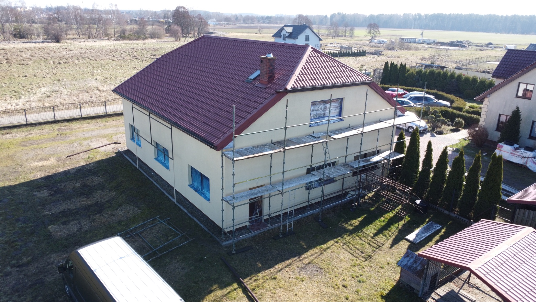 Dom jednorodzinny w trakcie malowania elewacji, okna zabezpieczone folią, rusztowanie przy ścianie, widok z góry.